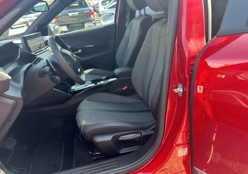 Vue intérieure côté conducteur d'un Peugeot 2008 rouge elixir 2025, avec sièges tissu et tableau de bord moderne.