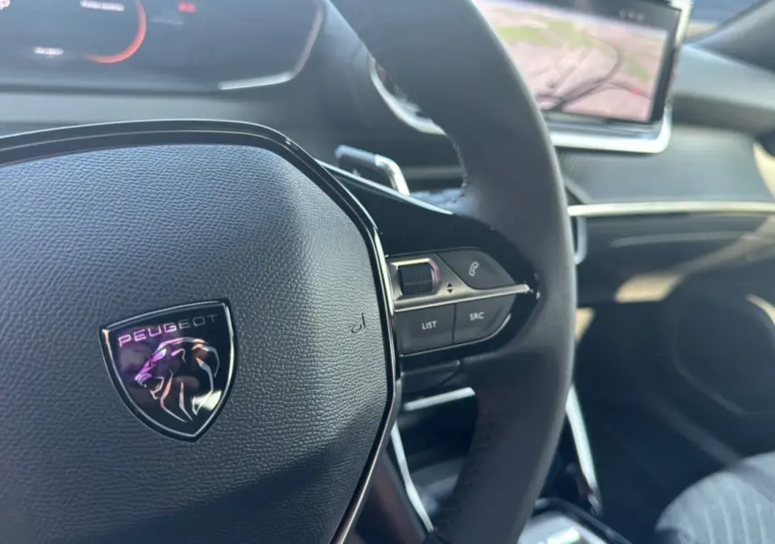 Gros plan sur le volant cuir multifonctions Peugeot 2008 Hybrid 145, avec tableau de bord et écran tactile en arrière-plan.