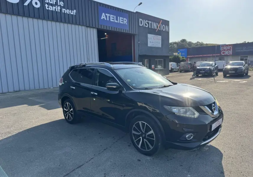 Nissan X-TRAIL III noir vu en 3/4 avant droit, avec jantes alliage et toit ouvrant, stationné devant un atelier.
