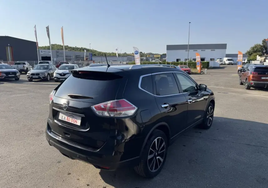 Nissan X-Trail noir vue 3/4 arrière droit, avec jantes alliage et vitres teintées, sur parking extérieur ensoleillé.