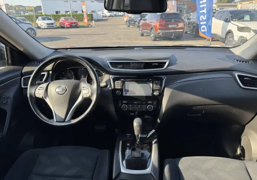Vue intérieure avant du Nissan X-TRAIL noir 2017, montrant le volant, la console centrale avec écran tactile et levier de boîte automatique.