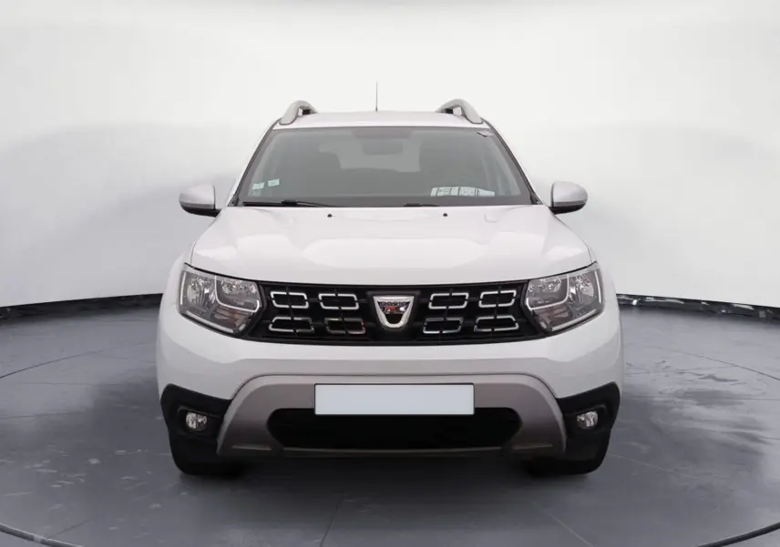 Vue de face du Dacia Duster blanc 2021, mettant en valeur sa calandre distinctive et ses phares LED allumés.