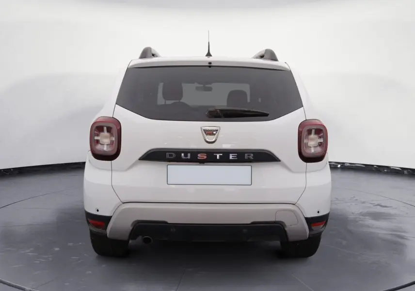 Vue arrière d'un Dacia Duster blanc 2021, avec feux arrière distinctifs et logo bien visible sur un terrain extérieur.