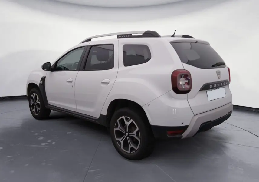 Vue arrière ouverte du Dacia Duster blanc 2021, coffre spacieux visible avec hayon relevé en extérieur.