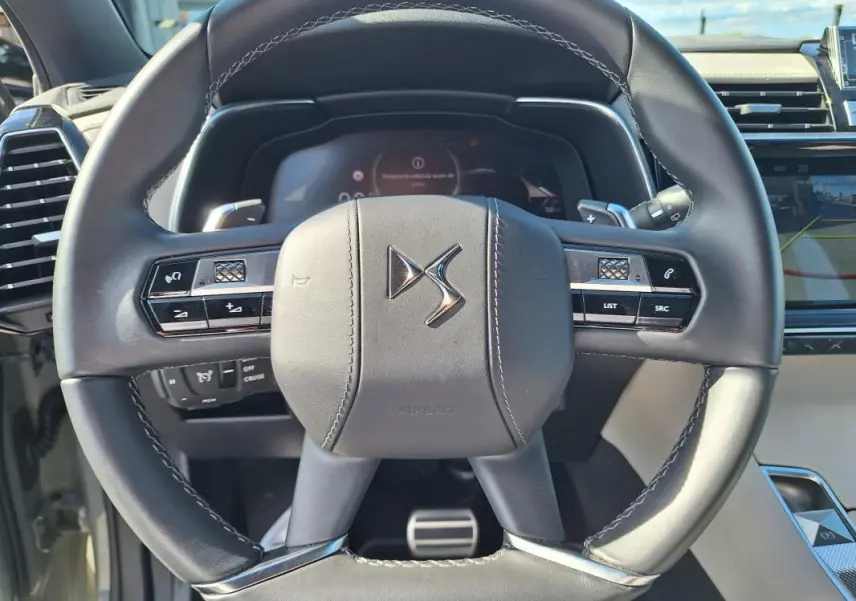 Vue rapprochée du volant en cuir noir du DS7 2024, avec commandes intégrées et tableau de bord numérique en arrière-plan.