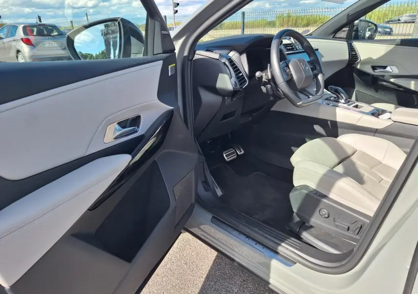 Intérieur clair vu côté conducteur d’un DS7 gris 2024, avec volant multifonction et sièges cuir beige.