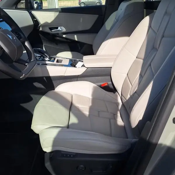 Vue intérieure côté conducteur du DS7 2024, sièges cuir beige, accoudoir central et volant multifonction.