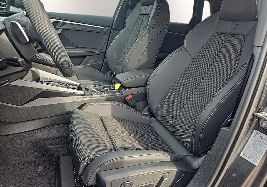Vue intérieure côté conducteur de l'Audi A3 Sportback 2026 avec sièges sport noirs et volant cuir multifonction.