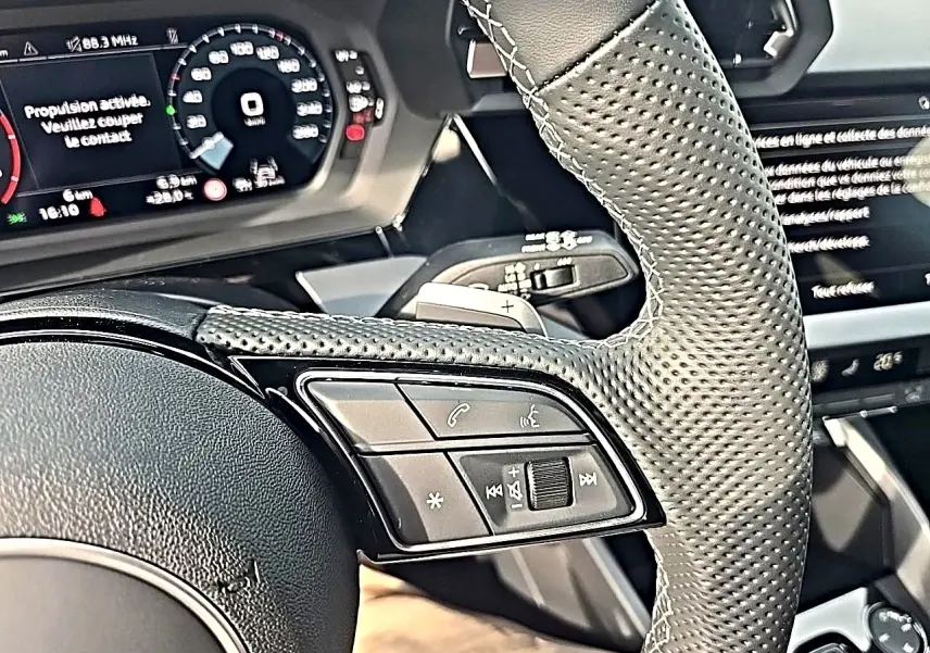 Gros plan sur le volant cuir perforé de l'Audi A3 Sportback 2026 avec commandes multifonctions et tableau de bord numérique.