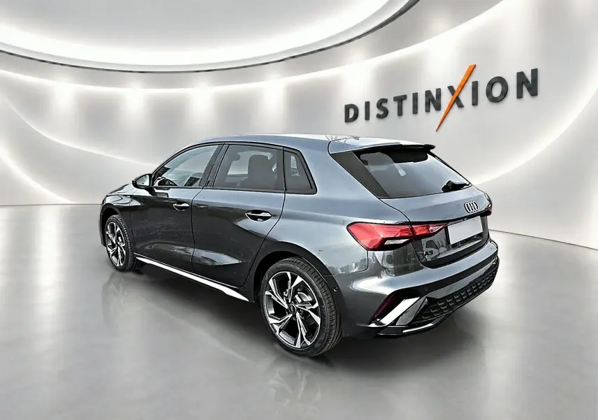 Audi A3 Sportback gris Daytona vue 3/4 arrière droit dans un showroom lumineux avec jantes alu noires et becquet arrière.