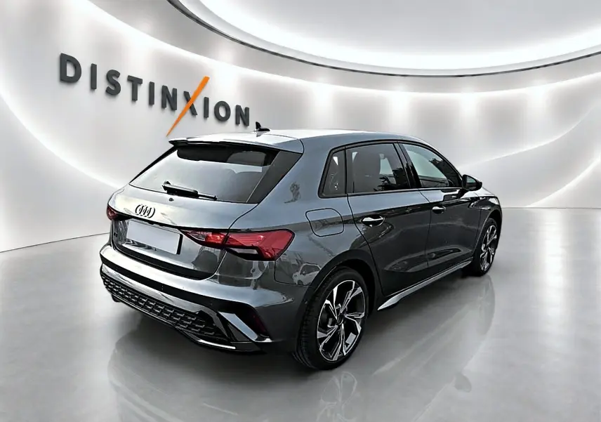 Audi A3 Sportback gris Daytona vue 3/4 arrière droit dans un showroom lumineux avec jantes alu distinctives.