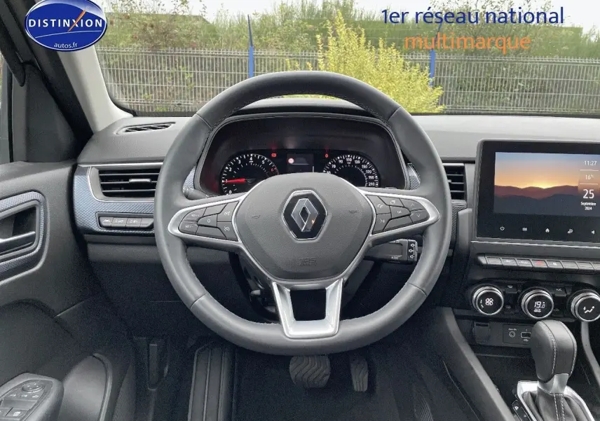 Vue intérieure centrée sur le volant Renault Arkana noir, tableau de bord et écran tactile lumineux en arrière-plan.