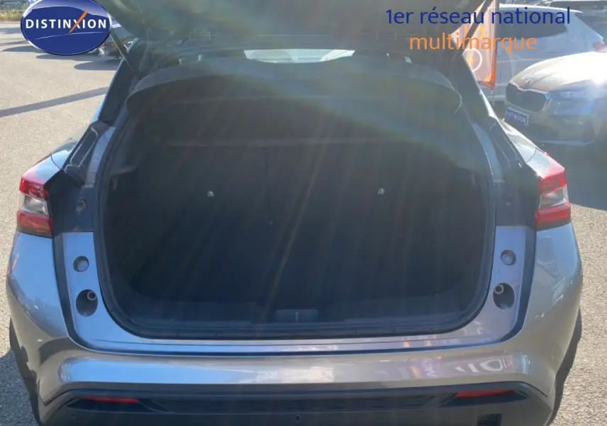 Vue arrière du coffre ouvert du Nissan Juke 1.6 Full Hybrid gris squale métal avec toit noir, en extérieur sous soleil.