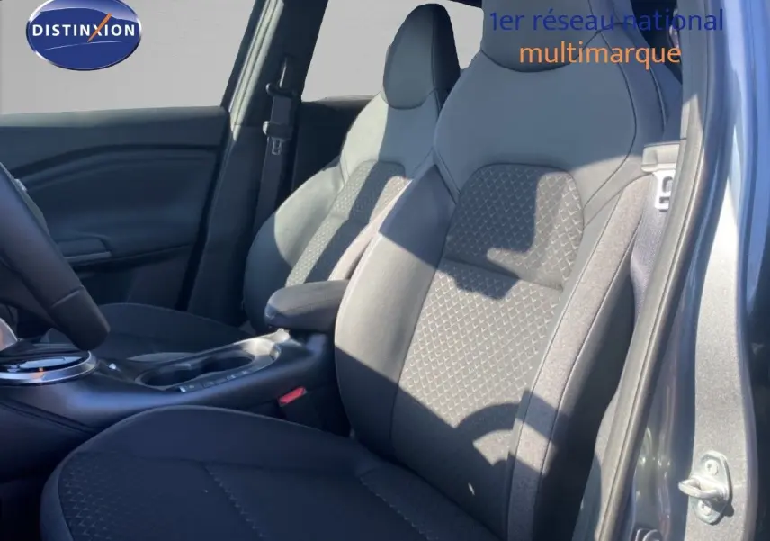Vue intérieure côté conducteur du Nissan Juke 2025, sièges tissu noir gris avec motifs géométriques et accoudoir central.