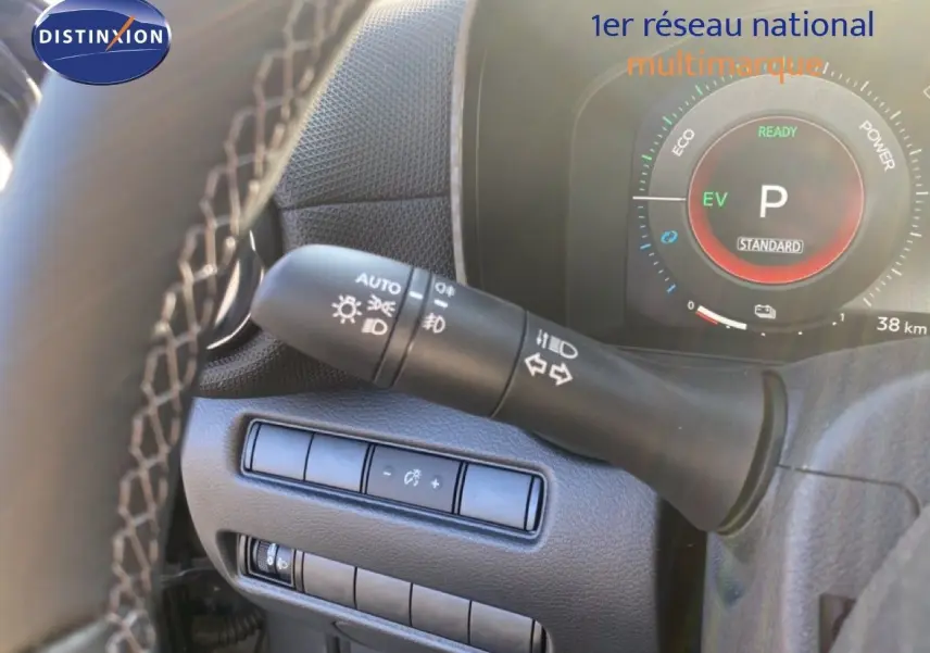 Gros plan sur le commodo d'éclairage et le tableau de bord numérique du Nissan Juke hybride, intérieur noir.