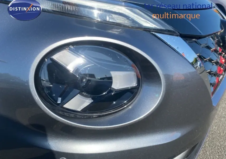 Gros plan sur le phare avant droit du Nissan Juke 2025 gris squale métal avec calandre noire brillante.
