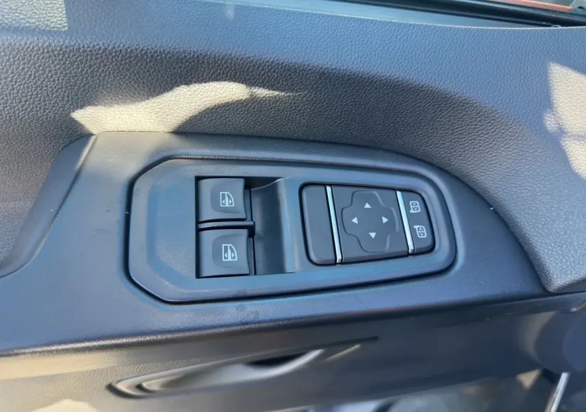 Gros plan sur les commandes électriques des vitres et rétroviseurs sur la porte intérieure côté conducteur du Renault Trafic Combi gris.