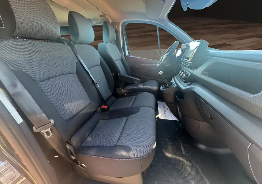 Vue intérieure côté conducteur du Renault Trafic Combi 2025, sièges tissu noir et tableau de bord avec écran tactile.