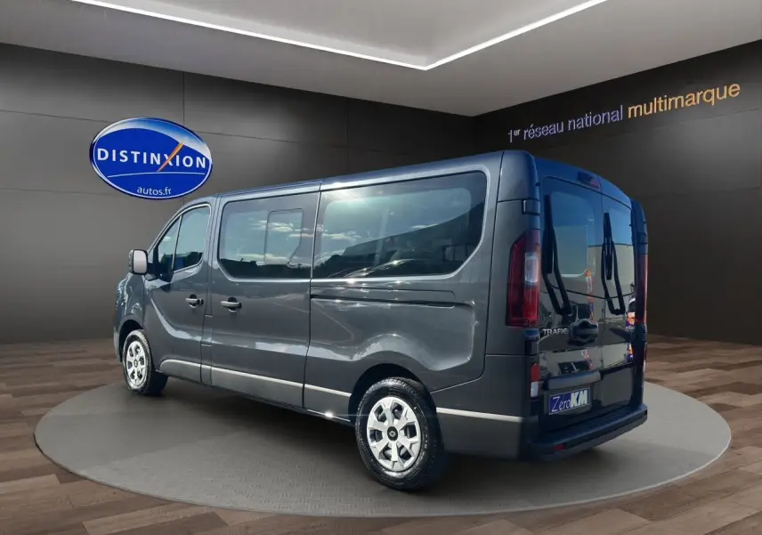 Vue 3/4 arrière droite d'un Renault Trafic Combi gris comète avec portes arrière vitrées dans un showroom.