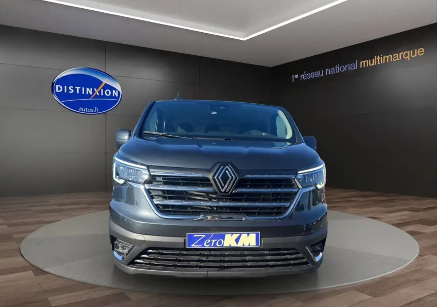 Renault Trafic Combi gris comète vu de face, avec calandre chromée et feux LED intégrés allumés.