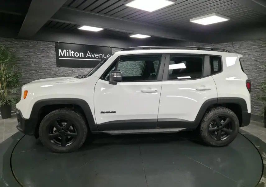 Profil côté gauche d'un Jeep Renegade blanc 2018 avec jantes noires 5 branches et barres de toit gris clair.