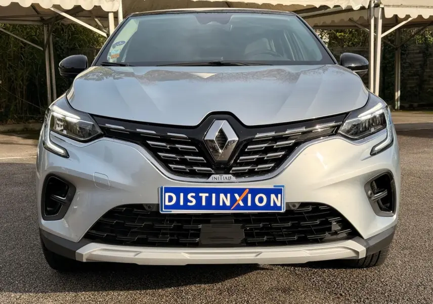 Vue frontale d'un Renault Captur gris Highland avec calandre noire et logo chromé sous un auvent.