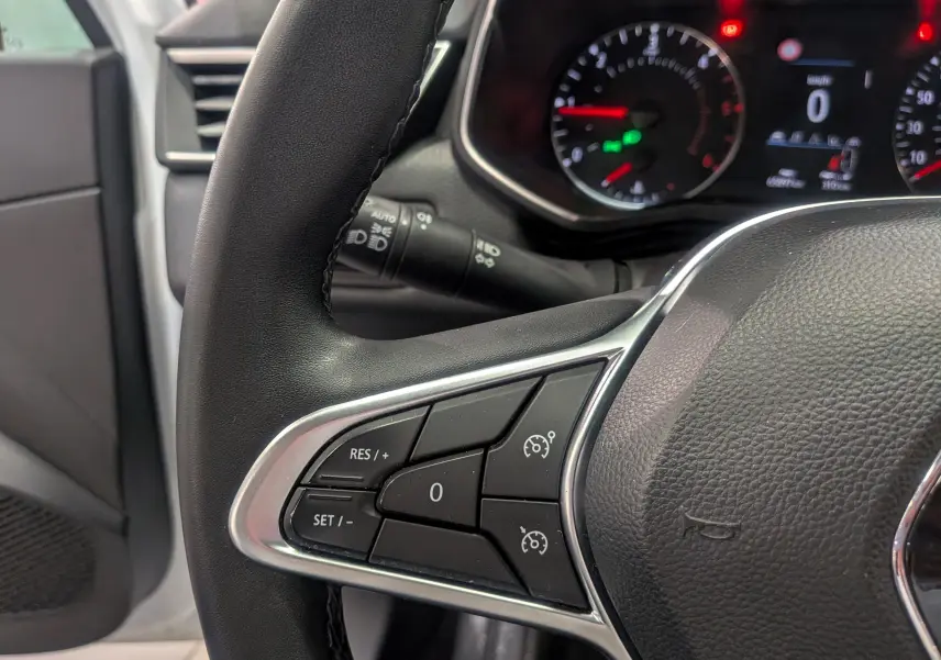 Gros plan sur le volant noir de la Renault Clio V, montrant les commandes de régulateur de vitesse et le tableau de bord en arrière-plan.