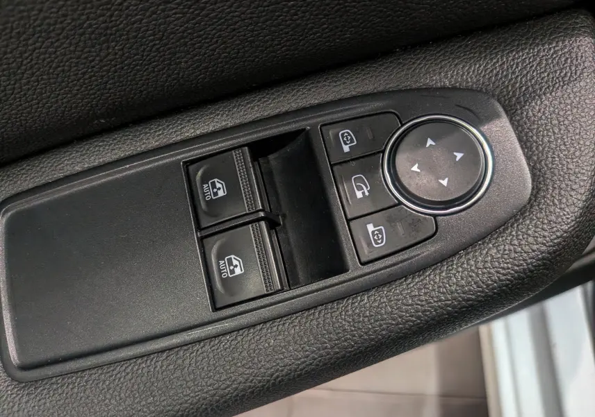 Gros plan sur les commandes de lève-vitres et réglage des rétroviseurs côté conducteur d'une Renault Clio V Blanc Glacier.