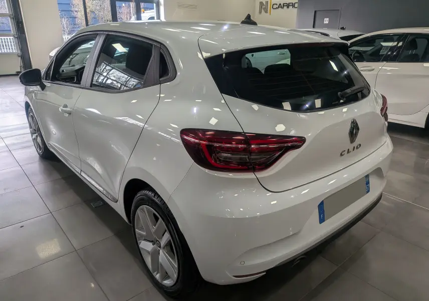 Vue 3/4 arrière droite d'une Renault Clio V Business blanc glacier, avec feux arrière LED et jantes alliage en showroom.