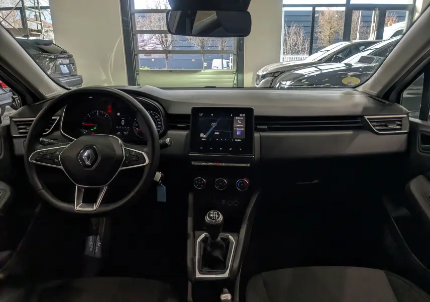 Vue intérieure frontale du tableau de bord de la Renault Clio V Business 2020 avec volant, écran tactile et levier de vitesses manuel.