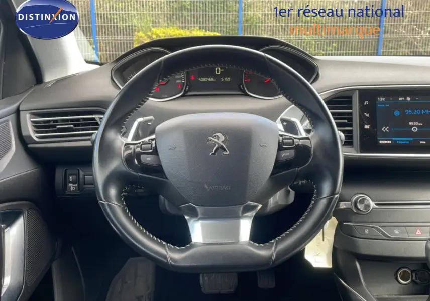 Vue intérieure centrée sur le volant cuir noir de la Peugeot 308 SW 2019 avec tableau de bord et écran multimédia.