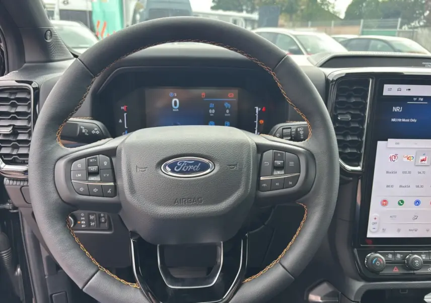 Vue rapprochée du volant cuir noir avec surpiqûres marron du Ford Ranger 2025, tableau de bord et écran tactile visibles.