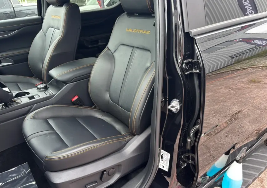 Vue intérieure côté conducteur du Ford Ranger Wildtrak 2025 noir agate, sièges cuir noirs avec surpiqûres orange et logo Wildtrak brodé.