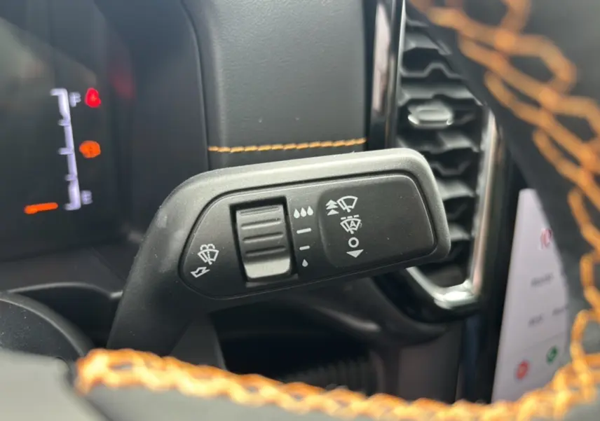 Gros plan sur la manette d’essuie-glace du Ford Ranger Wildtrak Plus noir avec surpiqûres orange du volant en cuir.