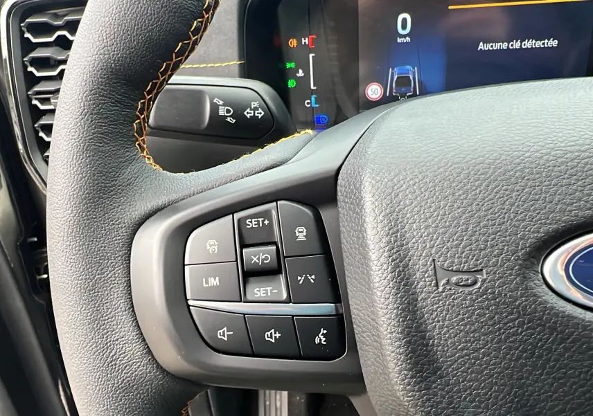 Gros plan sur le volant cuir noir du Ford Ranger 2026 avec commandes multifonctions et affichage digital en arrière-plan.