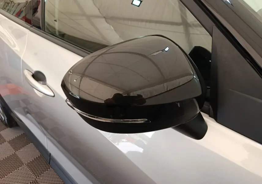 Rétroviseur côté gauche noir brillant sur Nissan Juke gris clair, vue rapprochée du côté conducteur.