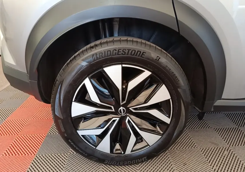 Gros plan sur la roue avant droite du Nissan Juke gris clair, jante alliage noir et argentée au design moderne.