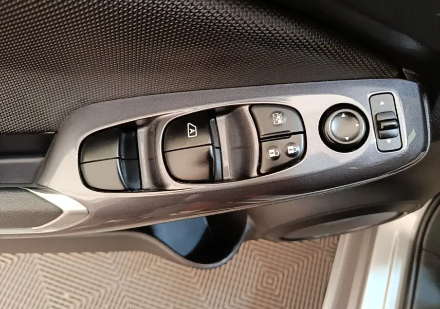 Gros plan sur les commandes de lève-vitres et rétroviseurs côté conducteur du Nissan Juke gris clair 2023.