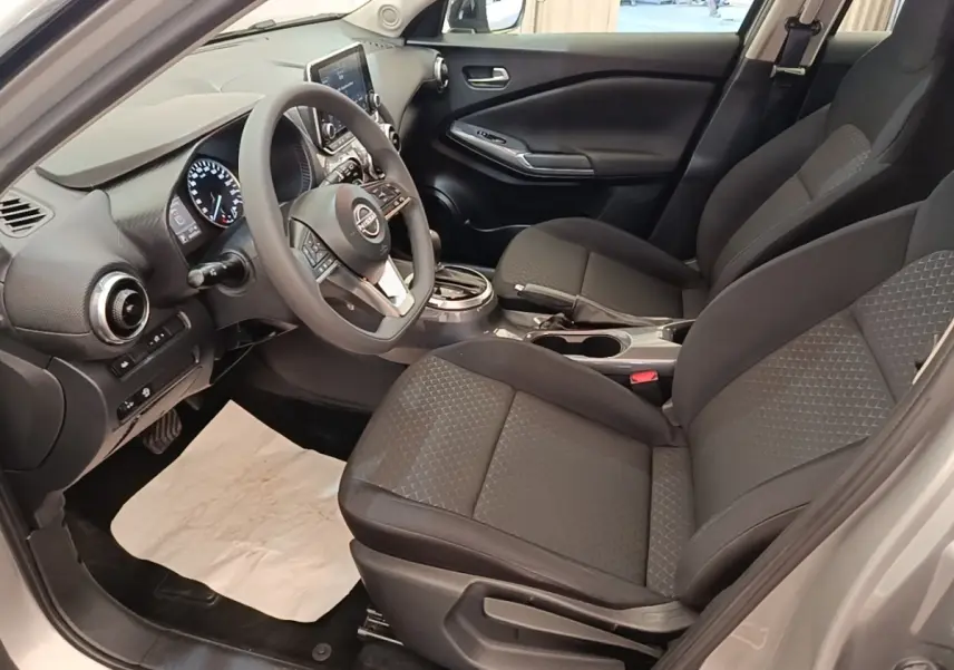 Vue intérieure côté conducteur du Nissan Juke gris clair 2023, avec tableau de bord digital et sièges tissu noirs.
