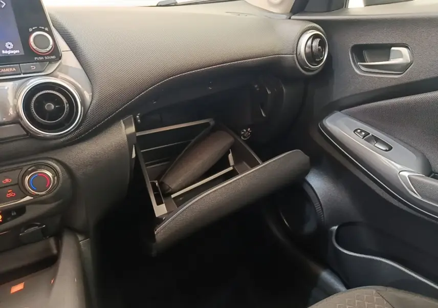 Intérieur noir du Nissan Juke 2023, vue côté passager avec boîte à gants ouverte et tableau de bord visible.
