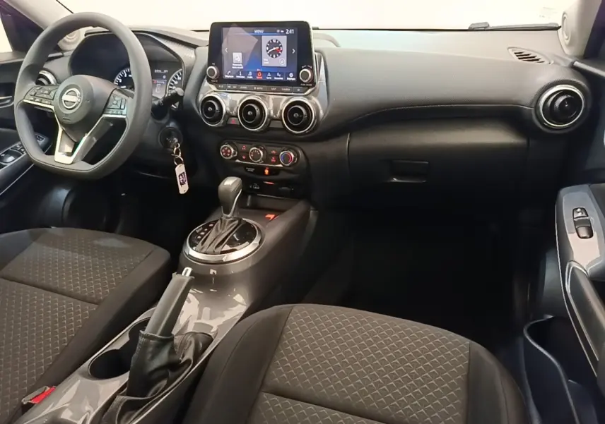 Vue intérieure avant du Nissan Juke gris clair 2023, avec tableau de bord central tactile et volant multifonctions.