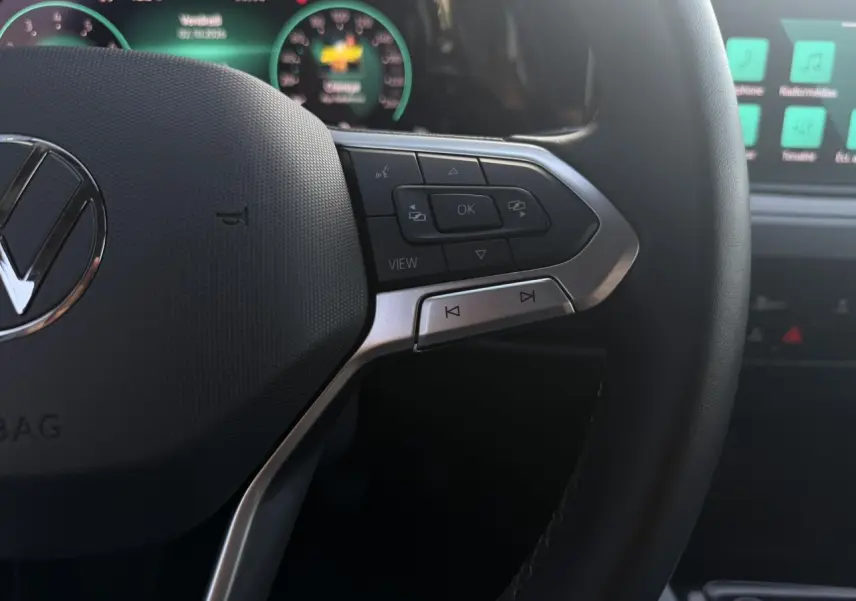 Gros plan sur le volant multifonction noir de la Volkswagen Golf VIII 2024, avec commandes intégrées et tableau de bord digital en arrière-plan.