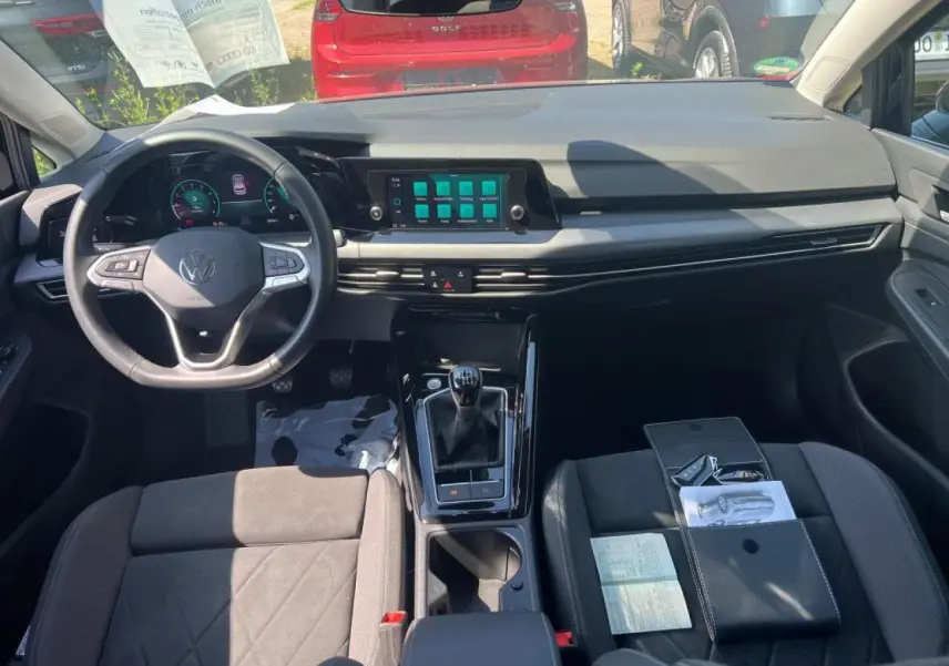 Vue intérieure avant de la Volkswagen Golf VIII noire, montrant le volant cuir multifonction et la boîte manuelle.