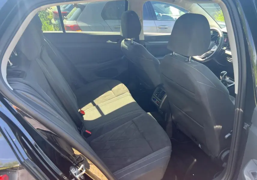 Vue intérieure arrière côté gauche de la Volkswagen Golf VIII noire, montrant les sièges arrière et avant en sellerie Microfleece.