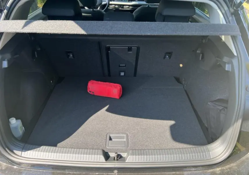 Vue du coffre ouvert d’une Volkswagen Golf VIII 1.5 TSI noire, montrant un espace de rangement avec trousse de secours rouge.