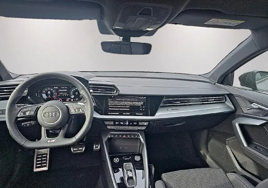 Vue avant de l’habitacle de l’Audi A3 Sportback 2026 avec tableau de bord noir et volant sport multifonction.