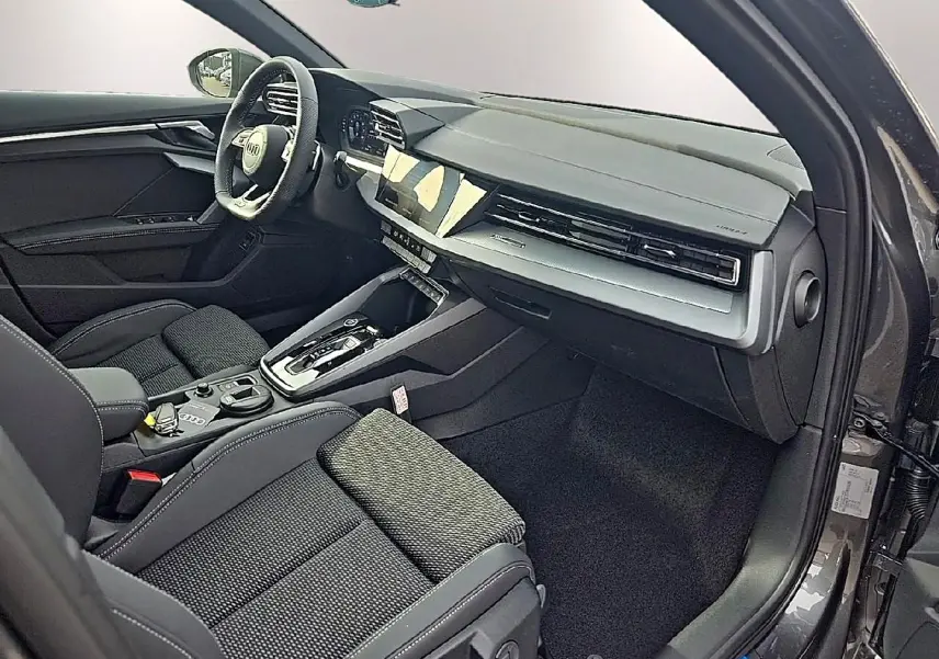 Vue intérieure côté passager avant d'une Audi A3 Sportback 2026 avec sellerie noire et tableau de bord moderne gris.