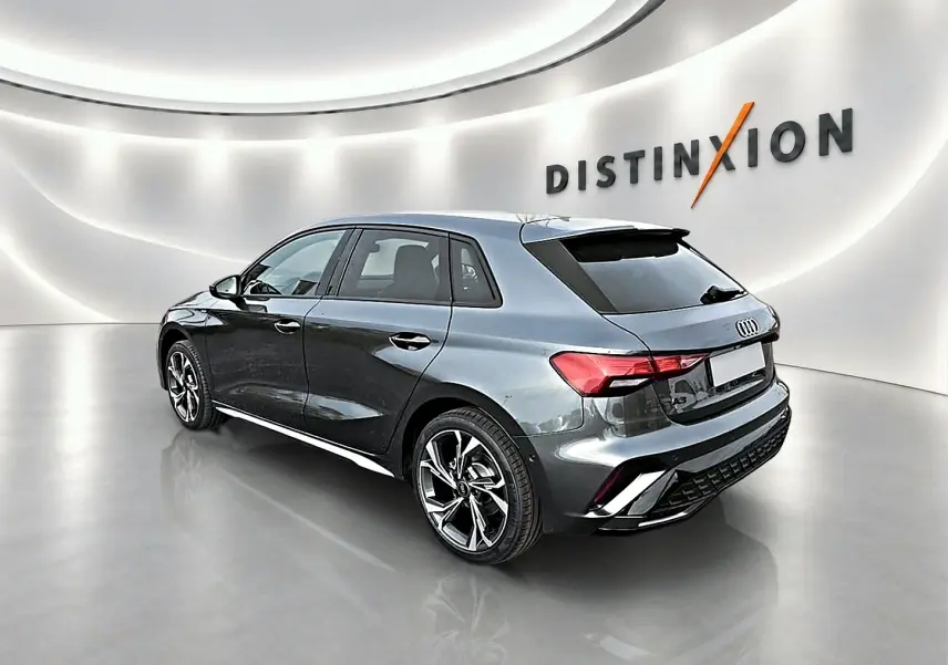 Audi A3 Sportback gris Daytona vue 3/4 arrière droit dans un showroom lumineux avec jantes alu noires.