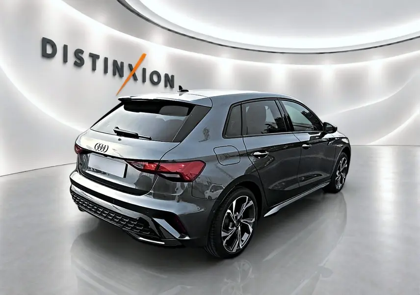Audi A3 Sportback gris Daytona vue 3/4 arrière droit dans un showroom lumineux avec jantes alu distinctives.