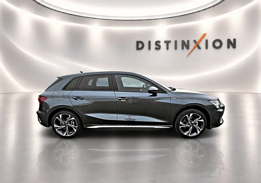 Audi A3 Sportback gris Daytona vue de profil côté gauche dans un showroom lumineux avec logo Distinxion en arrière-plan.